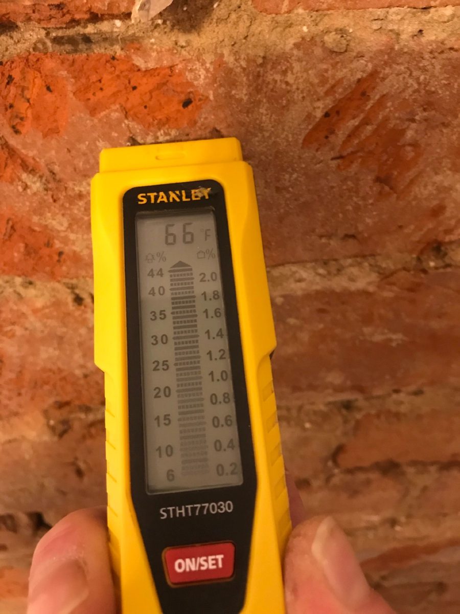 A hand-held moisture meter held against exposed brickwork, taking a reading