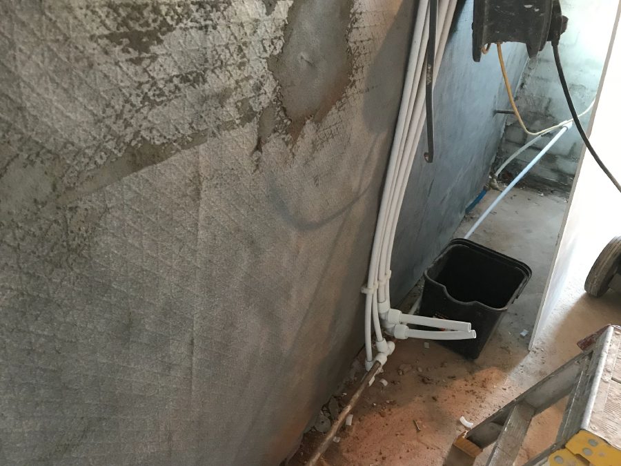 A wall part-covered in a new grey render coat, applied over bare masonry after damp treatment