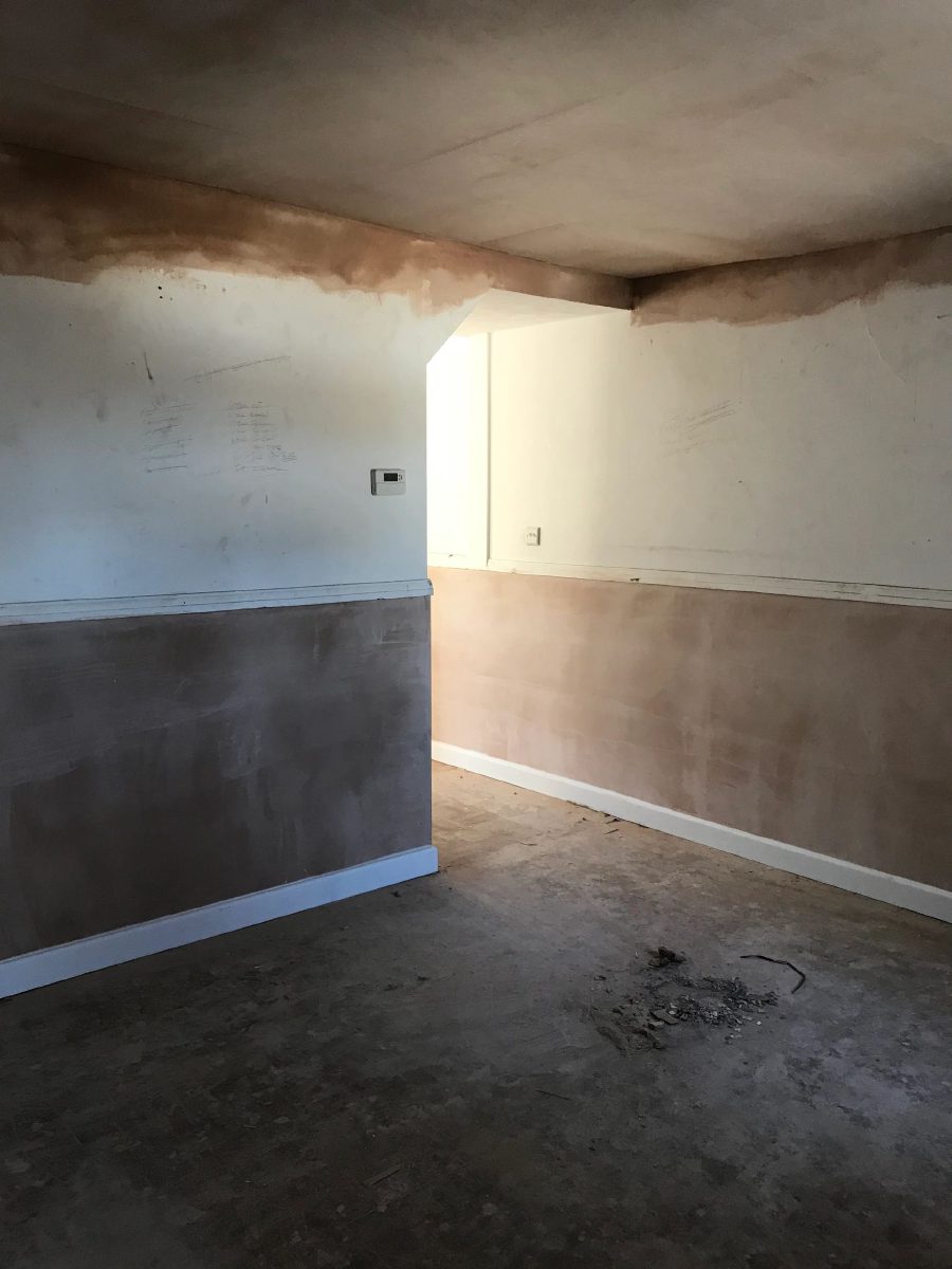 A room replastered after damp treatment, showing grey renovating render on the lower wall and pink finish plaster above