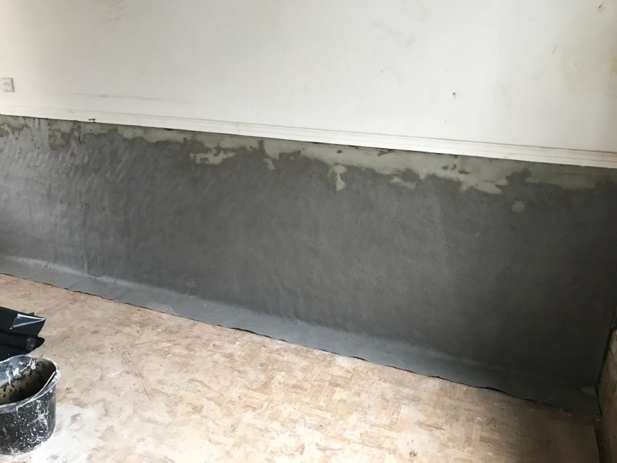 Grey tanking render across the lower half of a wall, dressed down onto a membrane at floor level